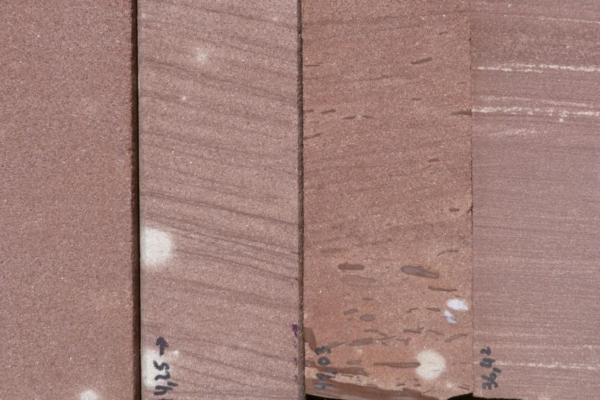 Das Foto zeigt vier hochkant nebeneinander stehende Gesteinsplatten. Alle haben eine rötlich graue Färbung, drei weisen jedoch schräg verlaufende oder waagrechte Streifen auf. Auch helle und dunkle Flecken sind sichtbar.