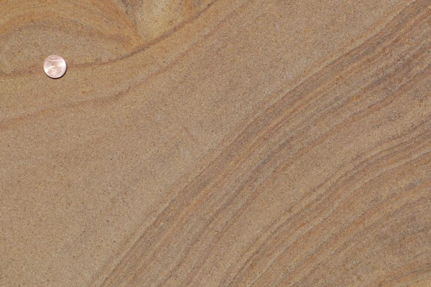Nahaufnahme einer hellbraunen Gesteinsoberfläche mit feiner, mehrfarbiger Bänderung rechts und größerer Zeichnung links oben. Ein dort ausgelegtes Centstück dient als Größenvergleich.