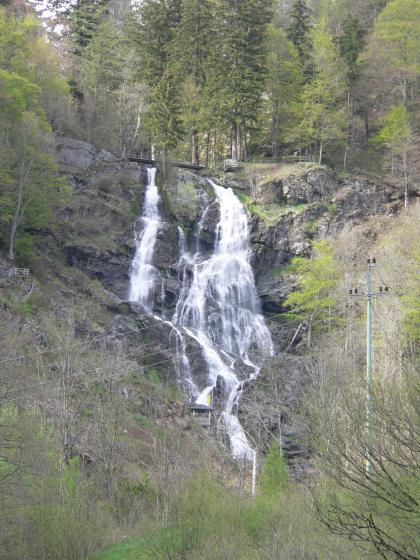 Aus einiger Entfernung blickt man hier auf einen Wasserfall, der sich aus großer Höhe über Felsstufen nach unten stürzt. Der oben aus zwei Strömen bestehende Wasserfall ist ringsum von Wald umgeben.