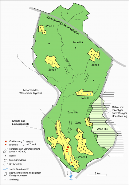 Blick auf eine mehrfarbige, vereinfacht ausgeführte Karte für ein beispielhaftes Wasserschutzgebiet mit Quellfassungen und Brunnen in einem Karstgrundwasserleiter.