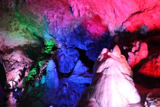 Blick in das Innere einer Höhle. Unterschiedliche Lichtquellen tauchen die Höhlenwände in rötliche, bläuliche und grünliche Farben.