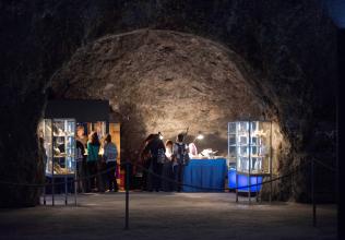 In einem höhlenartigen Raum sind mehrere Schaukästen und Verkaufstische mit Mineralien und Fossilien aufgestellt. Der Raum ist Teil eines Besucherbergwerks.