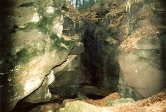 Das Foto zeigt eine höhlenartige Kluft zwischen graugrünen, teils abgerundeten und bemoosten Felswänden.