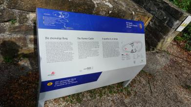 Blick auf eine abgeknickte, mehrfarbige Informationstafel aus Metall zur einstigen Burg auf dem Hohenstaufen bei Göppingen. Rechts ist eine Zeichnung vom Grundriss der Burg angebracht, links oben eine Wegskizze.