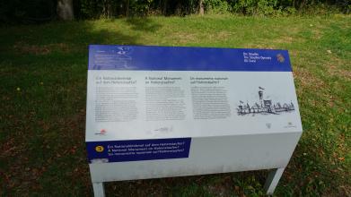Mehrfarbige Informationstafel aus Metall zum nicht realisierten Denkmal auf dem Hohenstaufen bei Göppingen. Rechts sieht man eine Zeichnung der früheren Burg auf dem Berg, links oben ist eine Wegbeschreibung angebracht.
