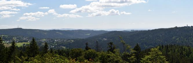 Blick von erhöhtem Standort über Waldspitzen, bewaldete Berge und dazwischen liegende teils bewaldete, teils besiedelte Hochflächen.