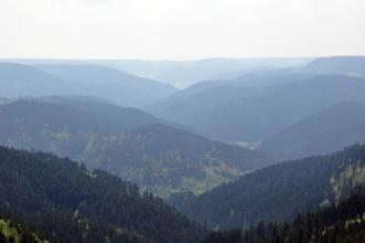 Ein aus großer Höhe gemachtes Bild, das mehrere hintereinander gestaffelte, bewaldete Berge zeigt.