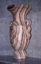Blick auf ein steinernes Gefäß mit Sockel, trichterförmiger Öffnung oben und seitlichen Haltegriffen. Das Gestein ist gelblich bis rötlich mit dunklen, senkrecht verlaufenden Streifen.