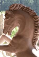 Das Foto zeigt eine aus rötlichem Stein gefertigte Skulptur. Zu sehen sind Kopf und Hals eines Pferdes mit wehender Mähne.