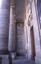 Das Foto zeigt den Eingangsbereich einer Kirche mit hohen Säulen links, Mittelwand und Portal rechts. Säulen und Wände des Gebäudes sind aus weißlich bis rötlich grauem Stein.