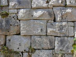 Das Bild zeigt eine Trockenmauer aus rechteckigen, hellgrauen Gesteinsblöcken. Die Blöcke haben alle eine leicht unterschiedliche Form. Manche Mauerfugen sind bewachsen.