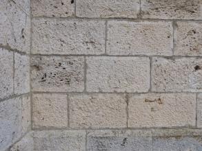 Großaufnahme einer Mauerecke aus hellgrauen Steinen. Die regelmäßig geformten Steine weisen eine raue Oberfläche und (in der Bildmitte links sowie am Bildrand) löchrige Vertiefungen auf.