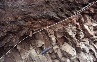 Blick auf flächiges, dunkles Gestein (links und oben) sowie bröckeliges, hellgraues Gestein (rechts sowie unten). Eine eingezeichnete schmale, diagonale Linie markiert die Grenze zwischen Grundgebirge und überlagernden Sedimentgesteinen.