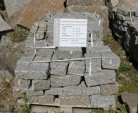 Das Bild zeigt einen Haufen zerkleinerter grauer Steinquader. Die Steine sind auf eine Holzpalette gestapelt und mit Spannbändern aus Metall gesichert. Ein aufgestelltes Schild gibt Hinweise zu Art und Größe der Steine.