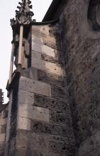 Teilansicht einer Kirchenwand mit linksseitig angebautem Strebepfeiler aus dunkelgrauen Mauersteinen. Teilweise sind auch hellgraue Steine verbaut.