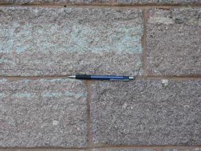 Teilansicht von Mauerwerk aus hellrotem bis violettem Gesteinsmaterial. In der Mitte ist ein Kugelschreiber als Maßstab platziert.