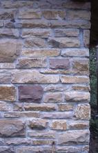 Teilansicht einer aus Steinen gefertigten Hauswand. Die Steine haben unterschiedliche Farben und Formen.