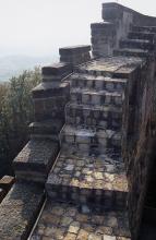 Blick auf eine treppenartig aufgebaute, hohe Burgmauer mit innenliegendem Treppenaufgang aus neueren Pflastersteinen.