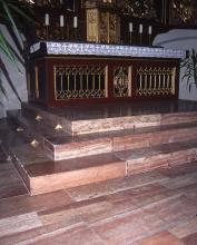 Blick in einen Kirchenraum mit vergoldetem Altar. Aufgang zum Altar über einen rötlich grauen Steinboden sowie steinerne Stufen.