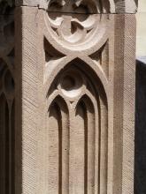 Teilansicht eines bearbeiteten Gesteinsblocks mit Kreuzblume und gotischem Fensterornament. Auffällig sind auch feine Löcher, die auf dem Stein verteilt sind.