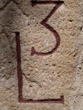 Nahaufnahme eines körnigen, porösen, hellbraunen Steinblockes mit dunkelrot gefärbten, eingravierten Markierungen (L und 3).
