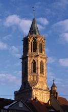Blick auf einen gotischen Kirchturm aus rötlichem Mauerwerk, von der Abendsonne angestrahlt.