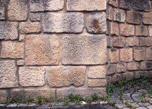 Blick auf eine Mauerecke aus unterschiedlich großen, rötlichen bis grauen Steinquadern.