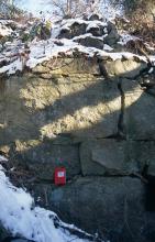 Teilansicht von grünlich grauem Gestein, durchzogen von dünnen Klüften und Rissen. Links unten sowie auf der Kuppe des Gesteins liegt Schnee.