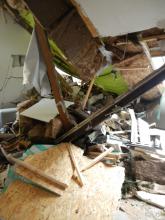 Das Bild zeigt die Zerstörungen in einem Wohnhaus nach einem Sturzereignis. Schutt, heruntergefallene Balken, Bretter und Dämmungsmaterial liegen über- und aufeinander. 