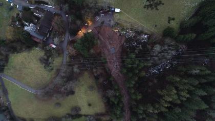 Luftbild Abrissbereich des Murganges (Foto: FB Drohne, Haberer, 2019) Die Luftaufnahme zeigt eine kleinteilige Landschaft, bestehend aus Wiesen, Gebäuden, Straßen und Wald. In der Bildmitte, innerhalb des bewaldeten Hangstückes, ist der Abriss- und Transportbereich des Murgangs zu erkennen.