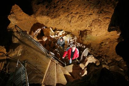 Laichinger Tiefenhöhle – Abstieg in die Kleine Halle in 55 m Tiefe; Foto: A. Schober/Archiv Höhlen- und Heimatverein Laichingen Blick von oben in den Schacht einer Höhle. Stein- und Metalltreppen führen Besucher von unteren Sohlen nach oben.