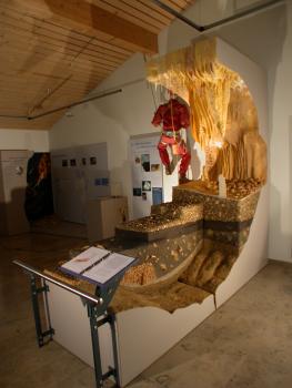 Im Museum für Höhlenkunde in Laichingen; Foto: A. Schober/Archiv Höhlen- und Heimatverein Laichingen Das Foto zeigt modellierte Gesteinsanschnitte einer Höhle. Rechts ist die im Bogen verlaufende Höhlendecke nachgebildet, mit abwärts hängenden Tropfsteinen. Im Hintergrund sind Schaubilder angebracht.