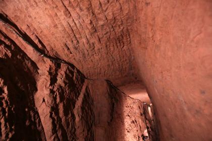 Schlägelspuren aus dem Spätmittelalter im Silberbergwerk Himmlisch Heer; Foto: Bergwerk Hallwangen Blick auf Wände und Decke in einem Bergwerksstollen. Im rötlich braunen Gestein sind oben deutliche Spuren von Bearbeitung mit Werkzeugen zu erkennen.
