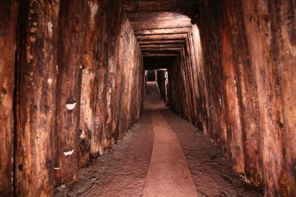 Türstock-Ausbau aus Holz im Besucherbergwerk Himmlisch Heer bei Dornstetten-Hallwangen; Foto: Bergwerk Hallwangen Blick in das Innere eines Bergwerks. Links und rechts des in der Mitte verlaufenden, teils mit Steinplatten ausgelegten Stollengangs sind Bohlen und Bretter aufgestellt. Auch die niedrige Decke sowie ein türartiger Durchgang werden von Holz gestützt.