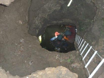 Erdfallschacht mit Zugang zur sog. Tannenäckerhöhle auf einer Wiese bei Allmendshofen, Schwarzwald-Baar-Kreis (Foto: GVV Umweltbüro Donaueschingen) Der Blick richtet sich von oben in ein tiefes Loch in einem grau-braunen Untergrund. In das Loch ist eine Leiter hinabgelassen. Man schaut von oben auf die Schutzhelme von zwei Personen die sich im Loch befinden.