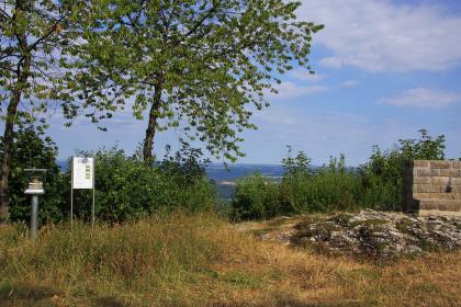 Aufschluss in der Lacunosamergel-Formation (Oberjura) an Station 22 des Geologischen Pfads Schwäbisch Gmünd-Hohenrechberg Erhöht liegender, von Bäumen und Gebüsch eingefasster Aussichtspunkt mit Felskuppe und Steinmauer rechts, einer Hinweistafel und Ausstellungsstücken links im Bild.