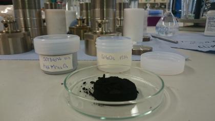 Laborversuche zu Gewinnung von Lithium (Quelle: EnBW Energie Baden-Württemberg AG) Das Bild zeigt im Vordergrund eine flache gläserne Schale, die eine dunkle Substanz enthält, sowie mehrere beschriftete Behälter. Im Hintergrund sind Einrichtungsgegenstände eines Labors zu erkennen.