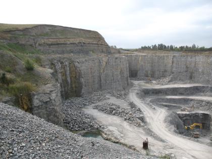 Oberer Muschelkalk und Unterkeuper, Vellberg Das Bild zeigt einen großen, zur rechten Bildhälfte geöffneten Steinbruch. Die steilen Wände bestehen aus grauem, im oberen Bereich horizontal geschichteten Gestein.