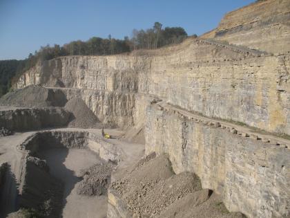 Oberer Muschelkalk und Unterkeuper, Frommenhausen Ansicht eines großen Steinbruchs mit mehreren Stufen, Fahrstraßen, Rampen und Schutthügeln. Das Gestein ist grau bis gelblich, die Böschung links bewaldet.
