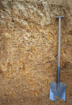 Älterer Lösslehm mit Frostmustern in der ehemaligen Lehmgrube am Blindenreisach nordöstlich von Weissach im Tal-Unterweissach Blick auf die rötlich braune Wand einer Lehmgrube mit bleichen Stellen und orange umrandeten Flecken. Ein angelehnter Spaten rechts im Bild zeigt die Größenverhältnisse an.