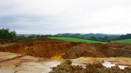 Sandgrube in den Goldshöfe-Sanden bei Rainau Blick auf eine Sandgrube mit rötlich brauner Rückwand links sowie Abraum rechts und im Vordergrund. Die Kuppe der Grubenwand ist bewachsen. Im Hintergrund folgen hügelige Wiesen und große Waldflächen.