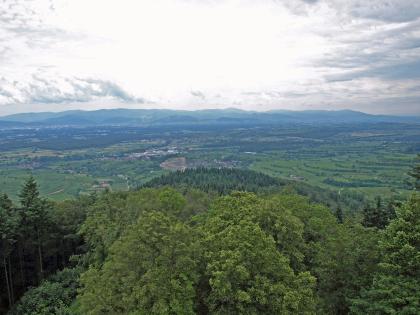 Blick vom Eichelspitzturm bei Eichstetten am Kaiserstuhl nach Südosten über den Phonolith-Steinbruch von Oberschaffhausen zum Hochschwarzwald Blick von erhötem Standort über eine bewaldete Bergkuppe auf weites, hügeliges, waldreiches Gelände mit Siedlungen und Rebterrassen. Im Bildmittelpunkt, unter den Ausläufern der Bergkuppe, ist zudem ein Steinbruck erkennbar.