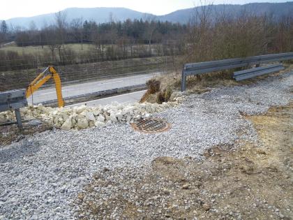 Dauerhafte Abfuhr des oberhalb der Böschung zuströmenden Wassers über eine feste Wasserführung zur Streckenentwässerung der A98 Zu sehen ist eine mit Schotter ausgelegte Fläche, in deren Mitte sich ein Gully befindet. Die Fläche grenzt an eine Böschung, unterhalb der eine mehrspurige Straße verläuft. Die Böschung ist am oberen Rand mit Leitplanken begrenzt.