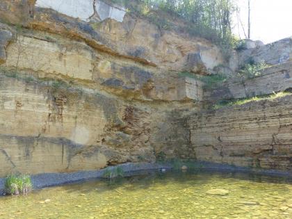 Ehemalige Abbauwand im Steinbruch der Firma Haas in Stuttgart Blick auf eine über Eck gehende ehemalige Steinbruchwand. Links sind drei mächtige Gesteinslager zu erkennen. Am Fuß der Abbauwände steht Wasser.