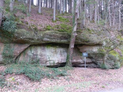 Felsböschung im Tiefenbachtal südwestlich von Schwäbisch Gmünd – Es handelt sich um eine natürliche Felsböschung in der Löwenstein-Formation (Stubensandstein) Mehrere hintereinander und aufeinander geschichtete, rötlich graue, teils längliche, teils wulstige Felsen bilden den Abschluss eines nach links ansteigenden, von Nadelbäumen bestandenen Waldhanges.