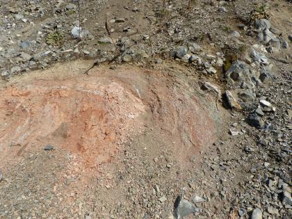 Basaltschlot Hohenstoffeln, Hilzingen Die Aufnahme zeigt einen steinigen, graubraunen Hangabschnitt. Links ist halbkreisförmig rötlicher Untergrund freigelegt.