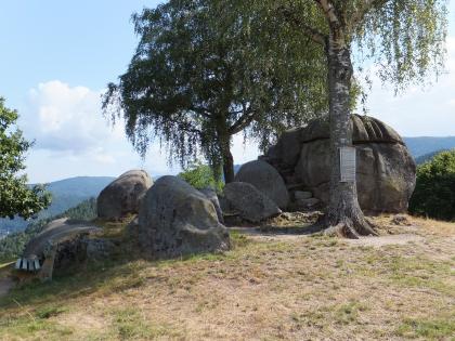 Die Giersteine bei Forbach-Bermersbach – Wollsackverwitterung im Forbach-Granit Blick auf mehrere große graue Steinblöcke. Die Blöcke liegen zwischen einzelnen Bäumen verstreut auf einer Bergkuppe. Der größte Block liegt rechts; eine kurze Steintreppe führt links daran hinauf.