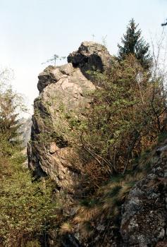 Falkenschrofen, Ottenhöfen im Schwarzwald Blick auf einen steilen, oben aufgesprengten Felsenturm. Das rötlich graue Gestein ragt hinter einem mit Gebüsch bewachsenen, nach rechts aufsteigenden Felshang hervor.