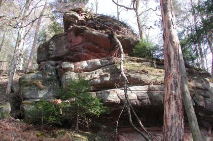 Großer Hochstein Blick auf ein pyramidenförmiges, treppenartig aufsteigendes Felsgebilde an einem Waldhang. Das Gestein ist im unteren Teil hellgrau, nach oben auch rötlich. Es gibt Nischen und Moosbewuchs, rechts liegt zudem ein langer Ast auf dem Fels.
