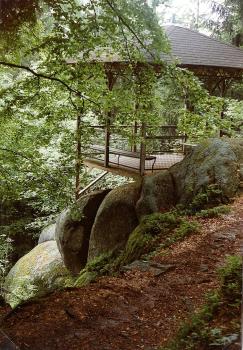 Dreikaiserfelsen, Triberg im Schwarzwald Blick auf einen nach links abfallenden Waldhang. Hangabwärts liegen große, gerundete Felsblöcke auf- und nebeneinander. Auf den oberen Blöcken ist eine hölzerne, überdachte Aussichtsplattform befestigt.